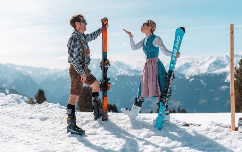 Mann & Frau in Tracht mit Ski im Schnee